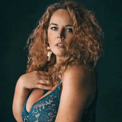 Dutchcurvesinheels poseert sensueel in blauwe kanten lingerie met hand op borst, vastgelegd in een donkere studiosetting.